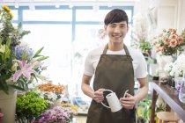 Chinese florist standing in flower shop with watering can — Stock Photo