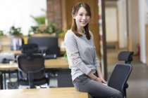 Китайська жінка, що сидить на столі в офісі — стокове фото