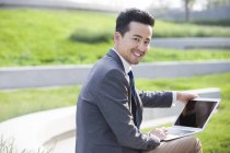 Chinese businessman using laptop in green area — Stock Photo