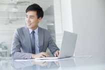 Hombre de negocios chino usando portátil en la oficina - foto de stock