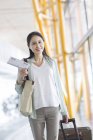 Mujer china madura caminando en el aeropuerto con maleta - foto de stock