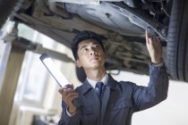 Chinese auto mechanic examining car with flashlight — Stock Photo