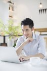 Chinese man using laptop in coffee shop — Stock Photo
