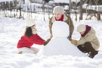 Padre chino y hermanos haciendo muñeco de nieve juntos - foto de stock