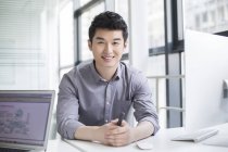 Китайский бизнесмен, сидящий в офисе с сжатыми руками — стоковое фото