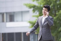 Chinese businessman talking on phone with suitcase — Stock Photo
