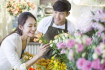Chinese woman smelling roses in store with florist — Stock Photo