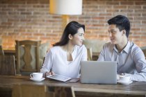 Chinese man and woman talking with laptop in cafe — Stock Photo