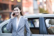 Китайська жінка, що мова йде про телефон перед автомобілем — стокове фото