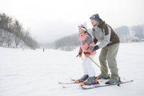 Китайский отец учит дочь кататься на лыжах на склоне — стоковое фото