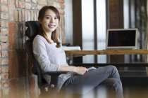 Mujer china sentada en silla en el escritorio en la oficina - foto de stock