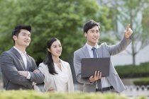 Chinese business people standing on street with laptop and pointing — Stock Photo