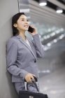Empresaria china apoyada en la pared y hablando por teléfono en el aeropuerto - foto de stock