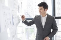 Chinesischer Geschäftsmann schreibt im Büro auf Whiteboard — Stockfoto