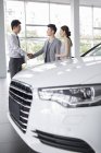 Китайская пара выбирает автомобиль с дилером в выставочном зале — стоковое фото