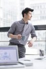 Chinese businessman standing with coffee in office — Stock Photo