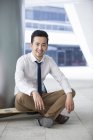Китайський бізнесмен, сидячи на скейтборді на стоянці — стокове фото