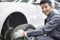 Mécanicien automobile chinois tenant roue de voiture dans l'atelier — Photo de stock