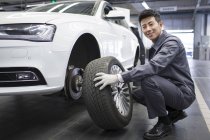 Chinese auto mechanic holding car wheel in workshop — Stock Photo