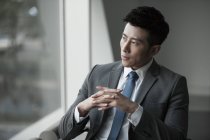 Homme d'affaires chinois regardant par la fenêtre dans le bureau — Photo de stock