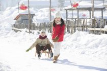 Chinese girl pulling sled with boy in snow — Stock Photo
