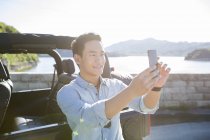 Chinese man taking selfie with smartphone in front of car — Stock Photo