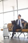 Empresário chinês sentado com laptop na sala de espera do aeroporto — Fotografia de Stock