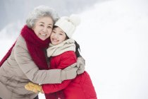Chinese grandmother and granddaughter embracing on snow — Stock Photo