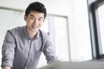 Chinesischer Geschäftsmann stützt sich im Büro auf Tisch — Stockfoto