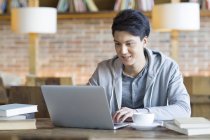 Chinese male student using laptop in cafe — Stock Photo