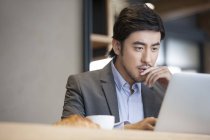Hombre de negocios chino usando el ordenador portátil en la cafetería - foto de stock