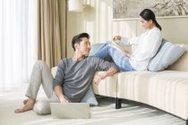 Casal chinês relaxante em casa com laptop e livro — Fotografia de Stock