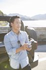 Chinese man standing with digital camera on lakeside — Stock Photo