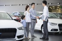 Chinese family shaking hands with car seller in showroom — Stock Photo