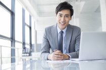 Uomo d'affari cinese seduto con computer portatile in ufficio — Foto stock