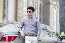 Chinese in sunglasses man leaning on car — Stock Photo