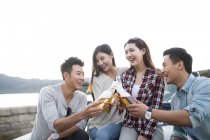 Chinese friends sitting on car with beer — Stock Photo