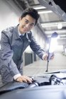 Chinese auto mechanic looking in camera while examining car engine — Stock Photo