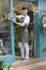 Chinese florist holding open sign in store doorway — Stock Photo