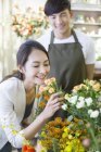 Chinese woman smelling roses in store with florist — Stock Photo
