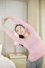 Chinês mulher em rosa sportswear alongamento no quarto — Fotografia de Stock