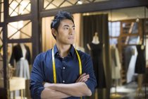 Chinesischer männlicher Modeschöpfer steht mit verschränkten Armen im Geschäft — Stockfoto