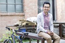 Hombre chino sentado en el banco con teléfono inteligente y bicicleta - foto de stock