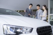 Chinese couple choosing car with dealer in showroom — Stock Photo