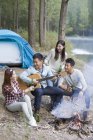 Chinese friends sitting around campfire and playing guitar — Stock Photo