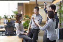 Chinese IT workers celebrating with smartphones in office — Stock Photo