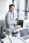 Chinese photographer sitting on desk in office — Stock Photo