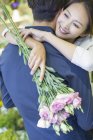 Chinese woman embracing boyfriend with flowers, close-up — Stock Photo