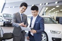 Chinesischer Geschäftsmann macht Deal mit Autoverkäufer im Showroom — Stockfoto
