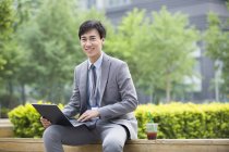Chinese businessman sitting with laptop on street — Stock Photo